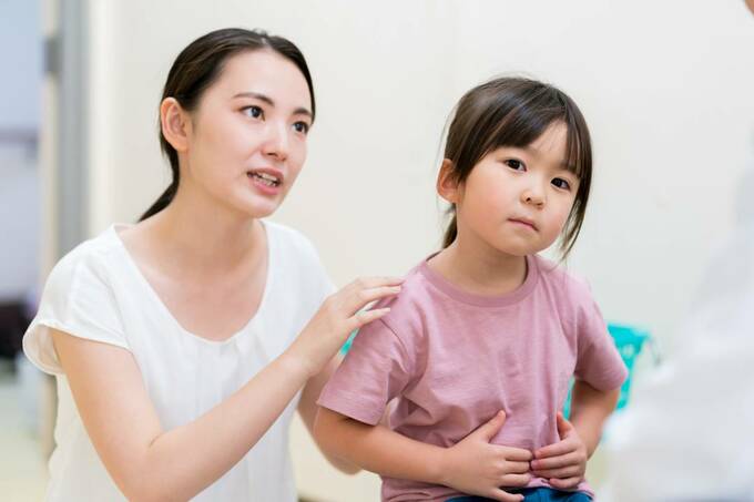 お腹をおさえる子どもの肩に手をおく女性