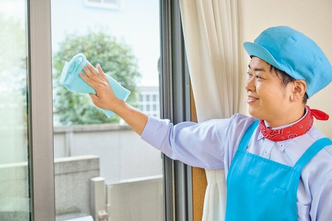 青いボディタオルで窓を拭いている青いエプロン姿の男性