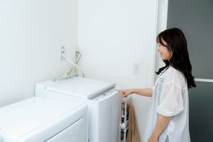 洗濯機の前に立つ白いトップスの女性