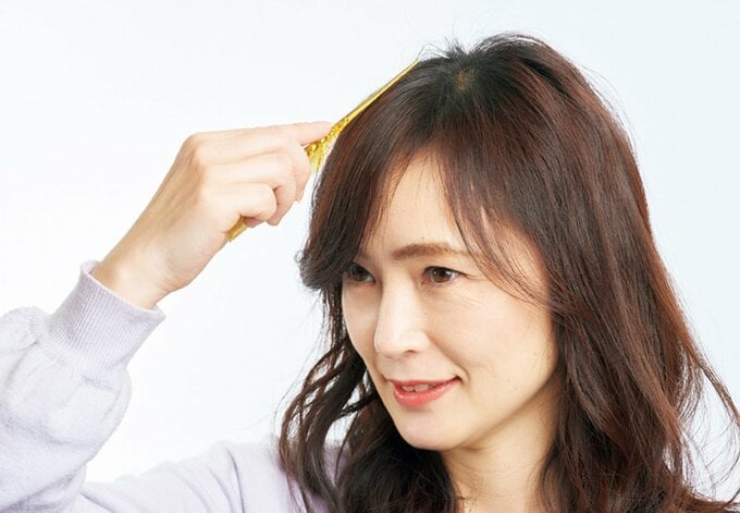 コームの柄の部分で頭頂部付近を押さえる女性