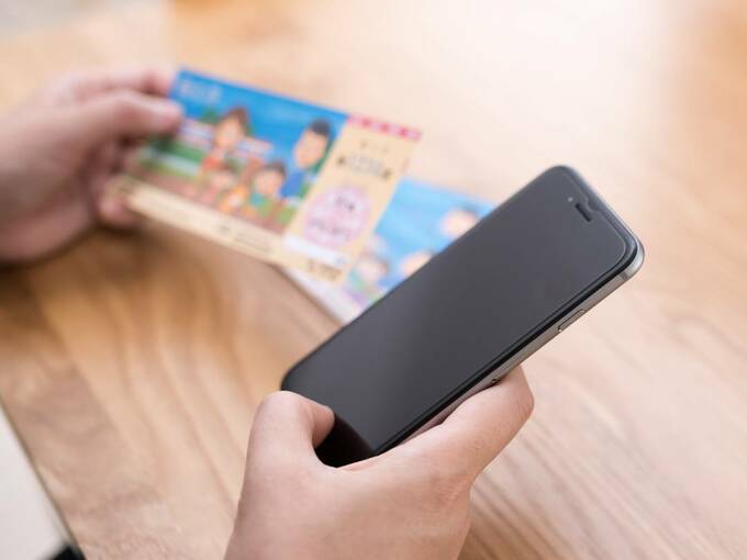 宝くじとスマホを片手に持つ