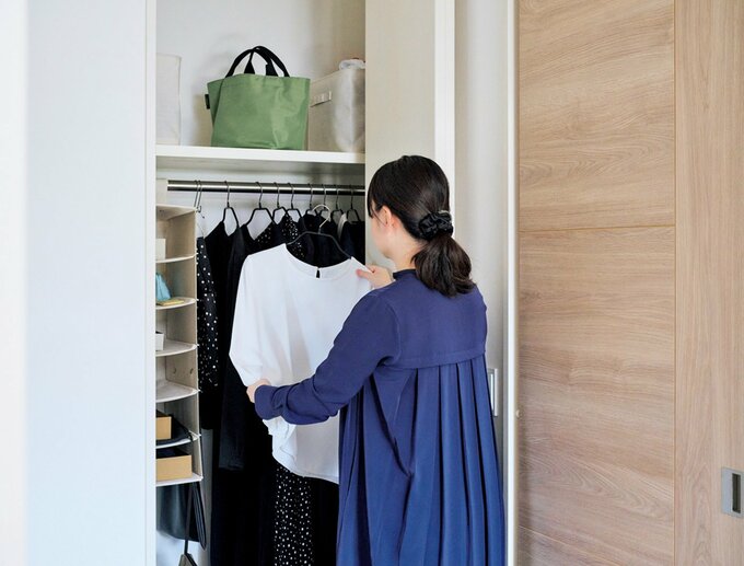 ネイビーのワンピースを着た女性がクローゼットの服を選ぶ様子