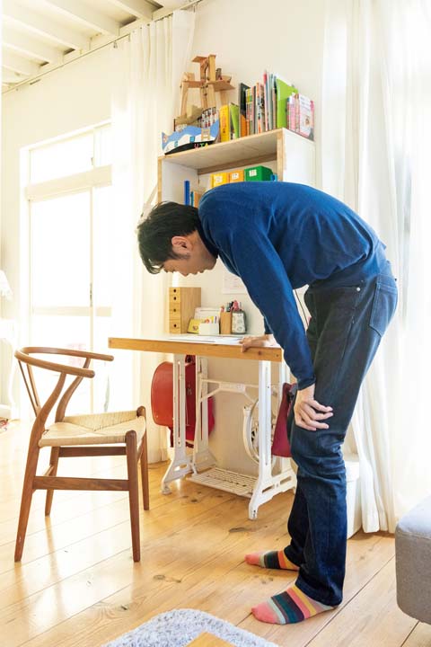 足踏みミシンを脚にした自作のテーブルを見る田中さん