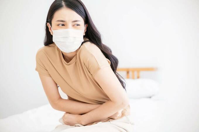 お腹をおさえるマスクをつけた女性