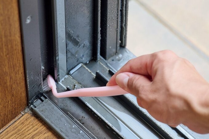 磨く部分を曲げたピンクの歯ブラシで窓のサッシを磨いている手元