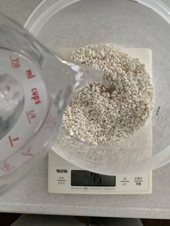 計量の上の米麹に水を加える様子