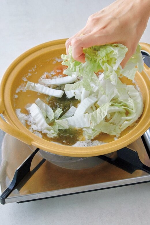 鶏肉を入れて煮立った鍋に白菜を入れている