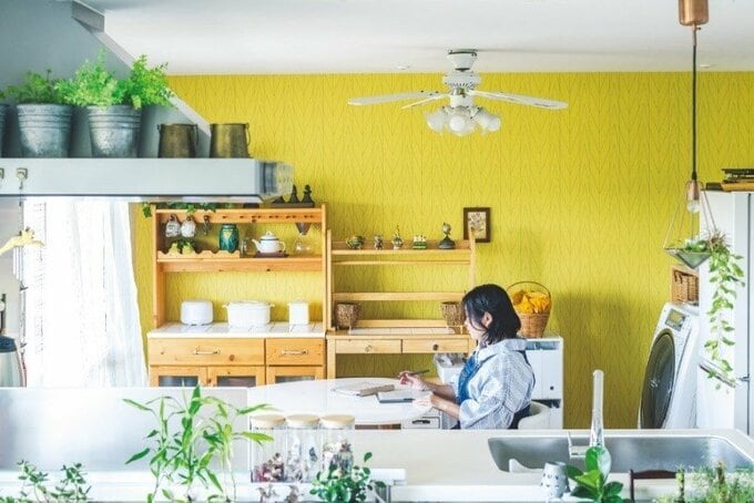 黄色い壁のダイニングの椅子に腰を据えて書き物をする女性