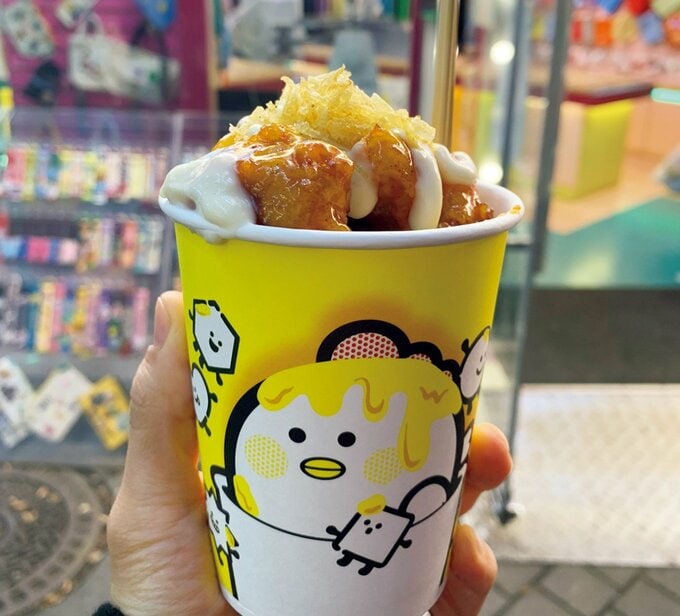 食べ歩きグルメのチキンが入った黄色い紙コップを持つ手元