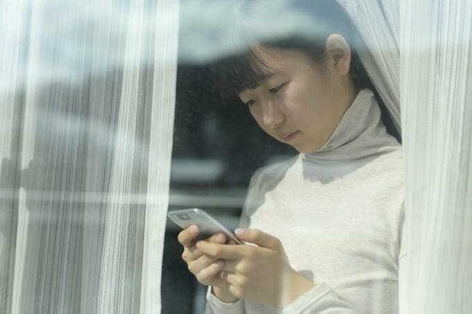 窓際にスマホを持つ女性