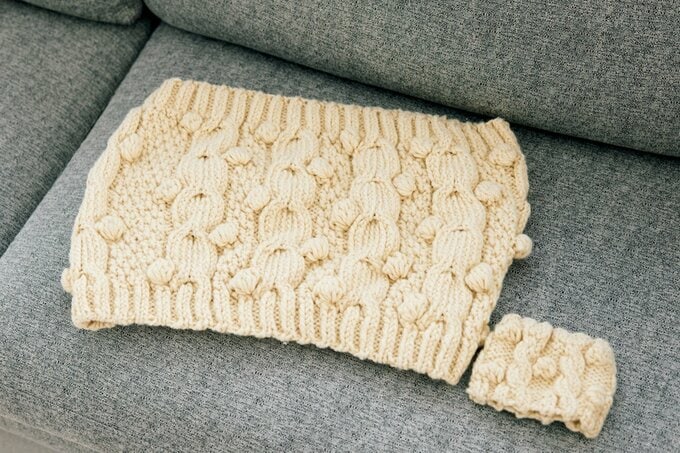 グレーのソファに置かれた白い糸で編んだネックウォーマー