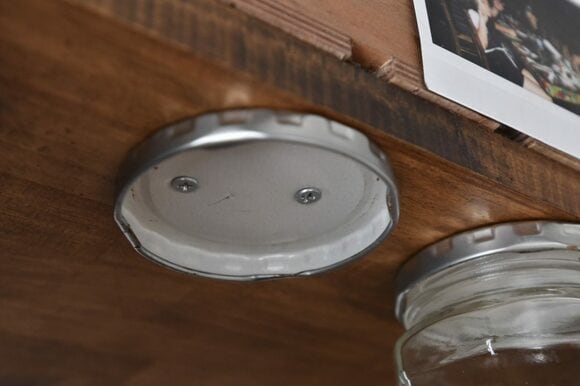 あきビンのフタをキッチンカウンターの棚裏にネジを使って固定。