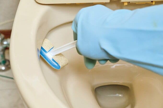 研磨剤つきスティックで便器のフチ裏を掃除している様子