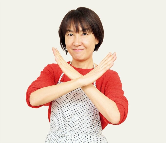 手で大きくバツポーズをとるエプロン姿の女性