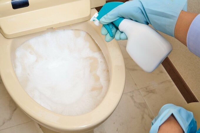 スプレー式泡タイプの塩素系漂白剤を便器に吹きかけている様子