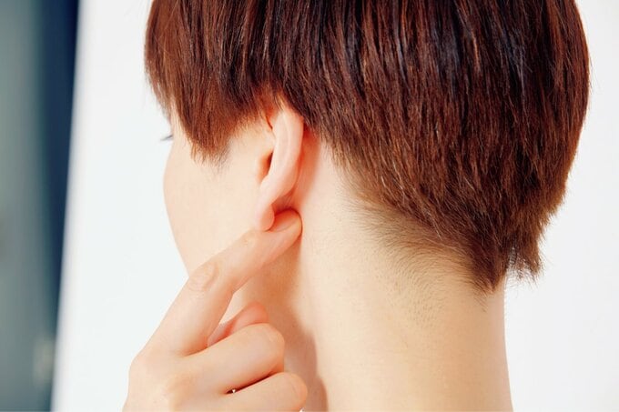 耳たぶの後をおさえる女性