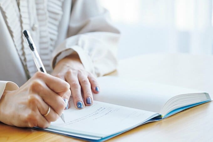 ノートに書きこみをしている青いネイルの女性の手元