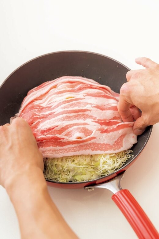 フライパンのキャベツに豚バラ肉を乗せる様子