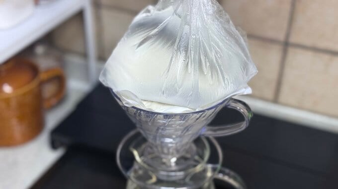 ヨーグルトの上にキッチンペーパーを置き、その上に重しとして水を入れたポリ袋を置いている