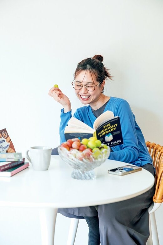 ブドウを食べながら読書をして微笑む、青いカーディガンの女性