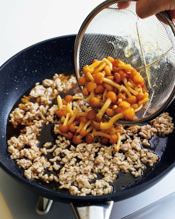 ひき肉が入ったフライパンにキノコを入れる様子