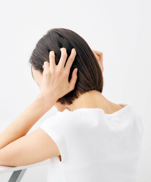 指で頭頂部に向けて後頭部を押し上げる女性