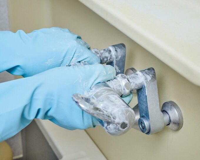 ゴム手袋をはめて、洗剤のついた蛇口を手で掃除している様子