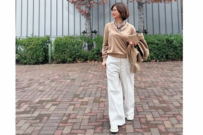 ベージュのトップスに白いパンツのきれいめファッションの女性