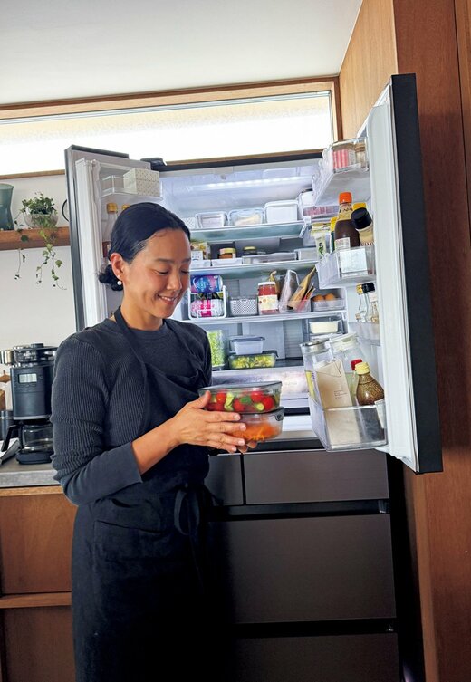 料理が入った保存容器を2つ持ち冷蔵庫の前に立つ女性