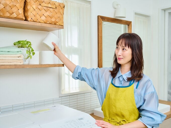 洗面所の棚にトイレットロールを収納する女性