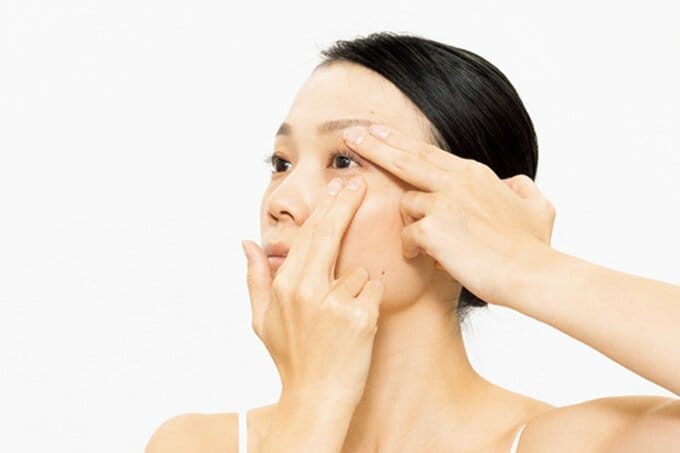 上下のまぶたに指を当てる女性