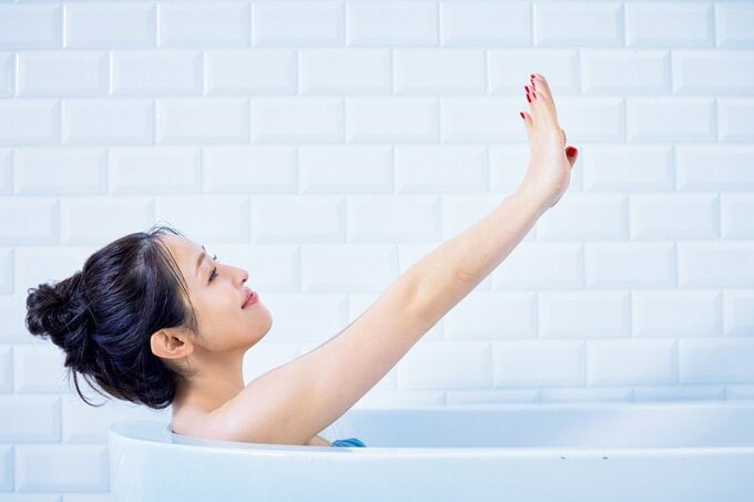 両手を伸ばす入浴中の女性
