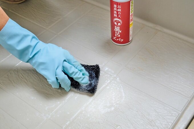 黒いスポンジで、浴室の床を磨いている様子