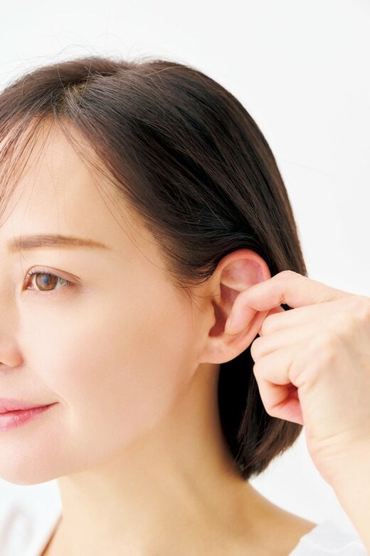 耳の真ん中を親指と人さし指ではさむ女性