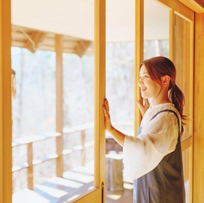 窓を開けながら外を眺めて微笑む女性