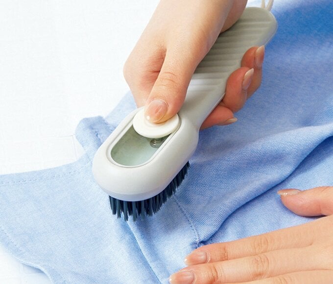 ブラシについたボタンを押しながら青いシャツの襟元を磨こうとしている手元