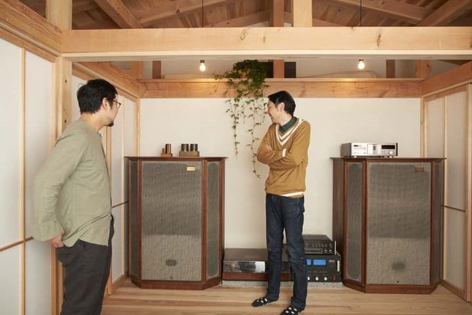 大きなスピーカーが鎮座する広いホールで会話をする村上さんと田中さん