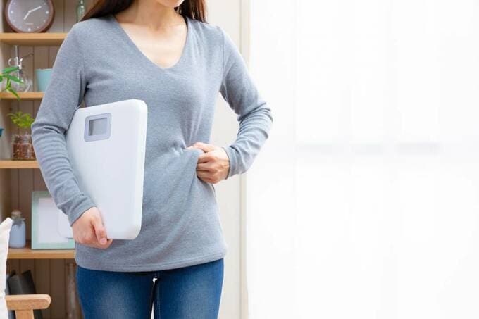 体重計を持ちながらお腹をつかむ女性