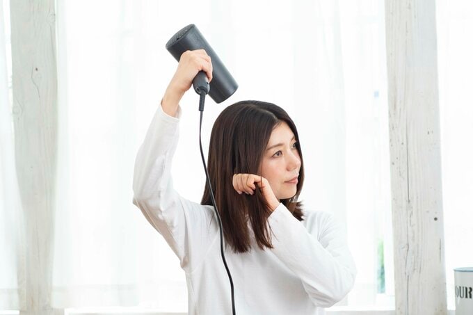女性がドライヤーの風を髪の毛にあてている