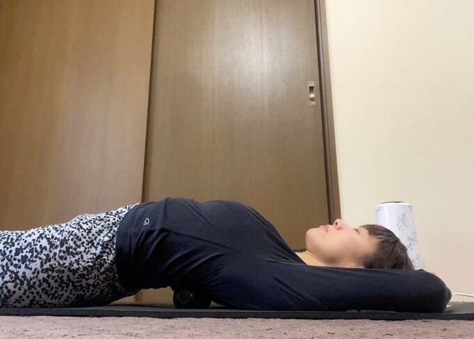 背中にツボ押しを置いて寝る女性