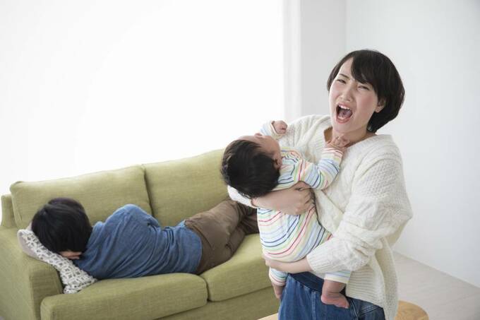 ソファで寝る男性と赤ちゃんをあやす女性