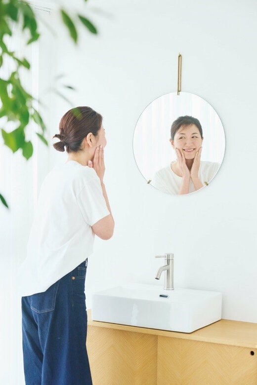 鏡を見ながら顔に手を当てて微笑む女性