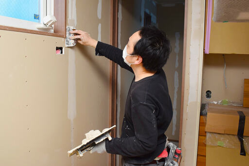 壁に塗られた余分なパテを削ぎ落としている職人さん