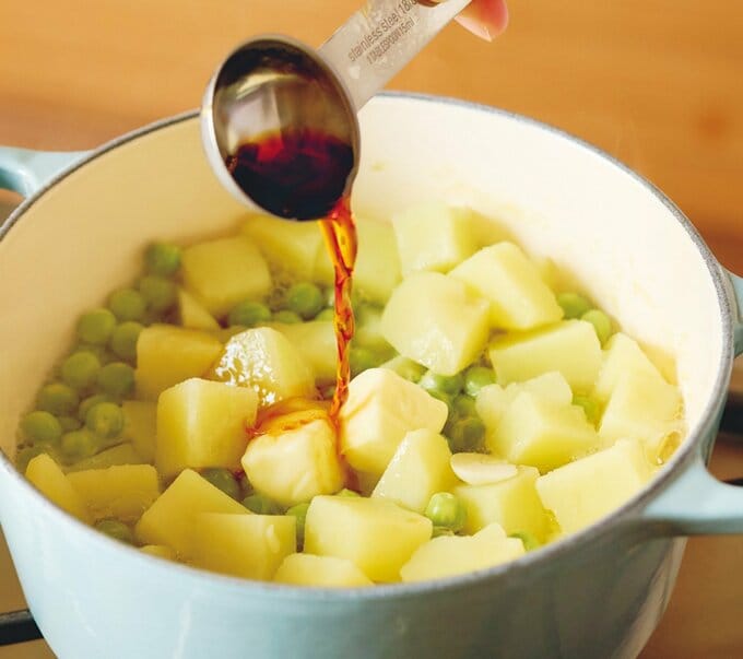 新ジャガイモとグリンピースが入っている鍋にしょうゆを入れる