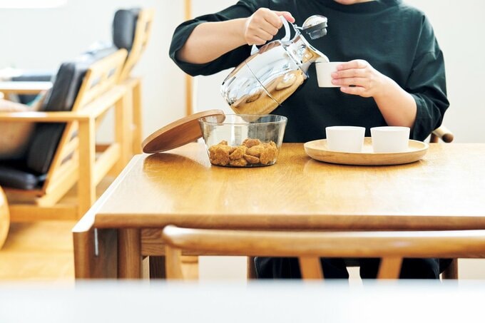 ダイニングテーブルに座ってお茶を入れる女性