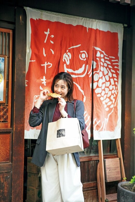 店の前でたい焼きを頬張るジャケットを着た女性