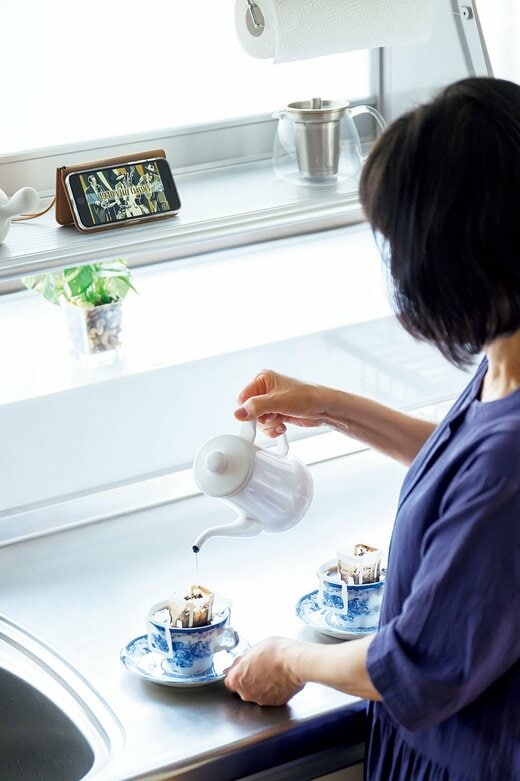 スマホ見ながらコーヒー注ぐ女性写真