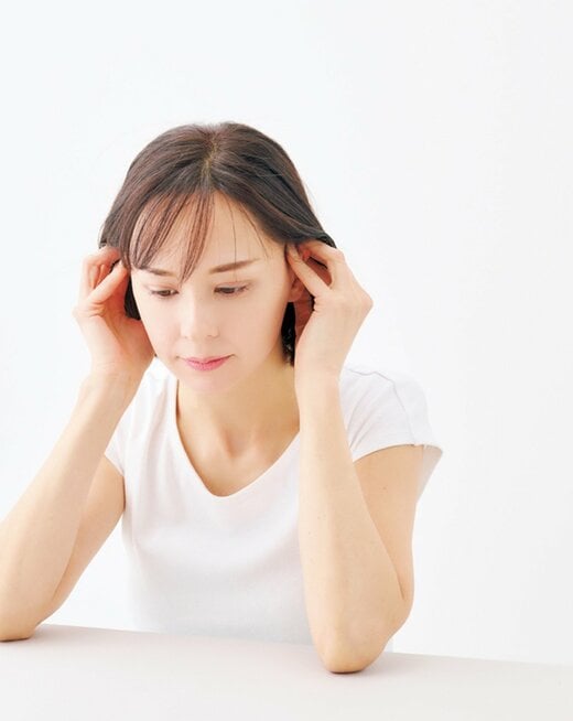 テーブルに肘をついて耳の付け根辺りを指で押し上げる女性