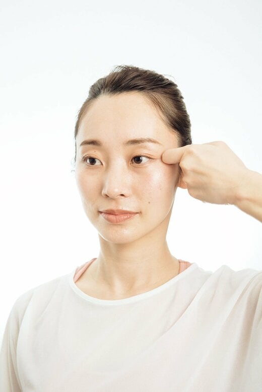 人さし指をカギの手にして、目尻に当てる