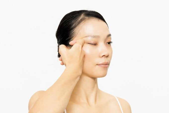 顔に指をあて片目を閉じる女性